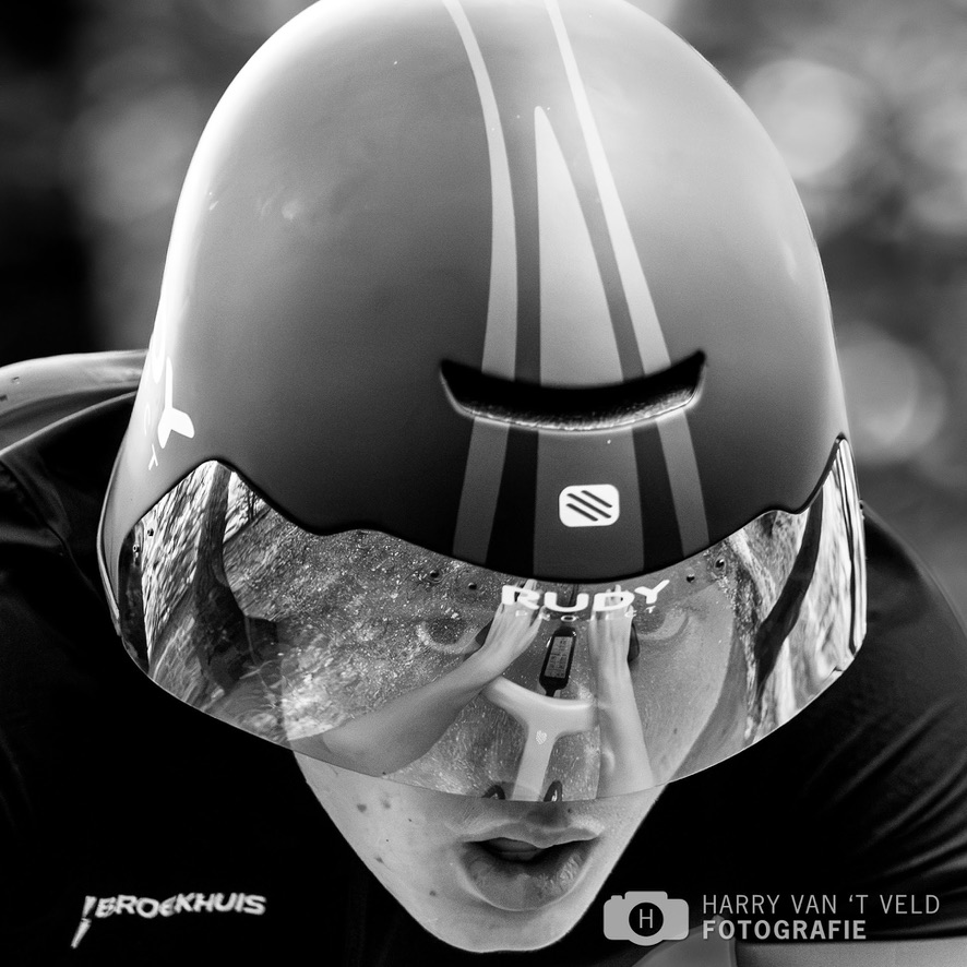 Black-and-white close-up of a time-trial cyclist wearing an aerodynamic helmet and reflective visor